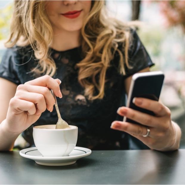 Junge Frau mit Handy in der Hand und trinkt Kaffee