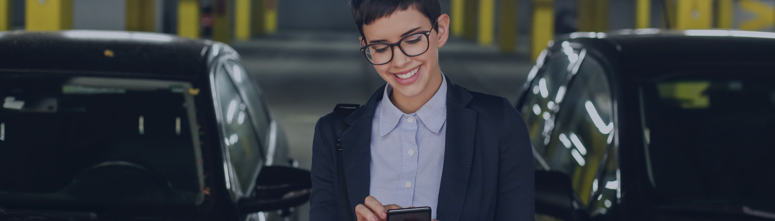 Frau mit Brille und Mobiltelefon in der Hand in einer Tiefgarage Frau mit Brille und Mobiltelefon in der Hand in einer Tiefgarage